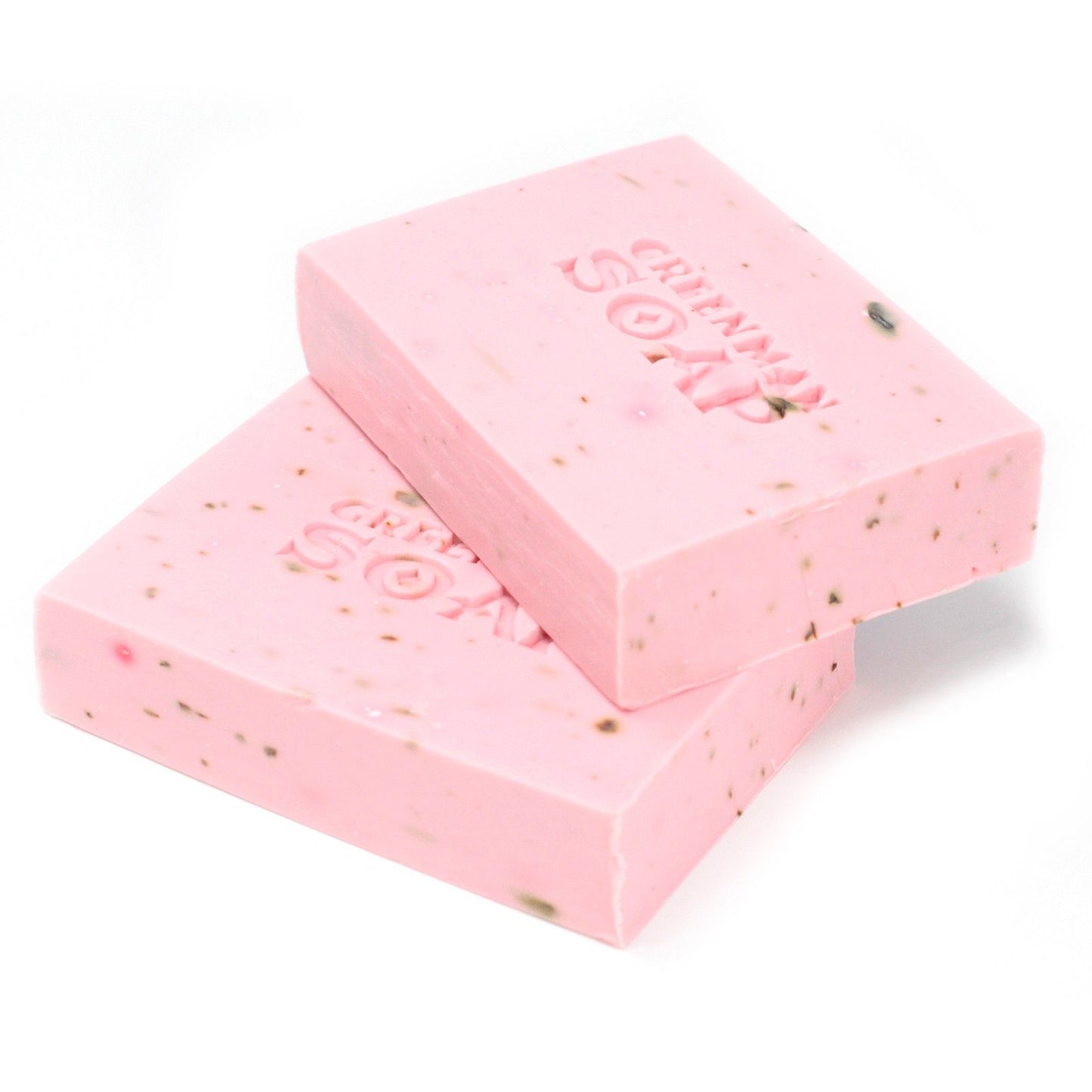 Dos pastillas de jabón rosa claro con motas oscuras y la inscripción "GREENMAN SOAP" grabada en relieve.