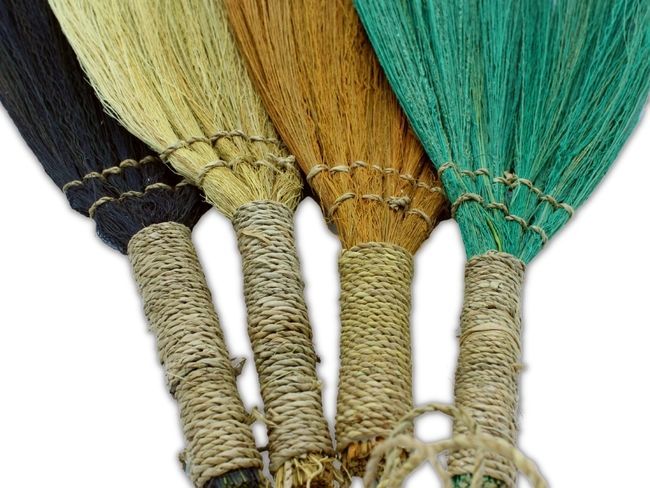 Escobas de colores naturales: negro, dorado, marrón y verde, con mangos de yute trenzado, estilo artesanal.