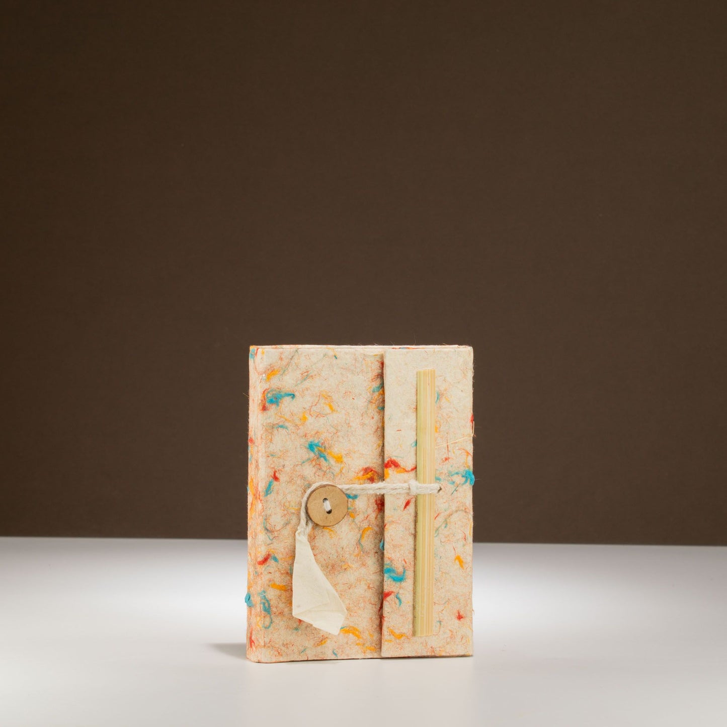 Cuaderno artesanal con tapa de papel reciclado en tonos beige y detalles de colores, cierre con botón de madera.