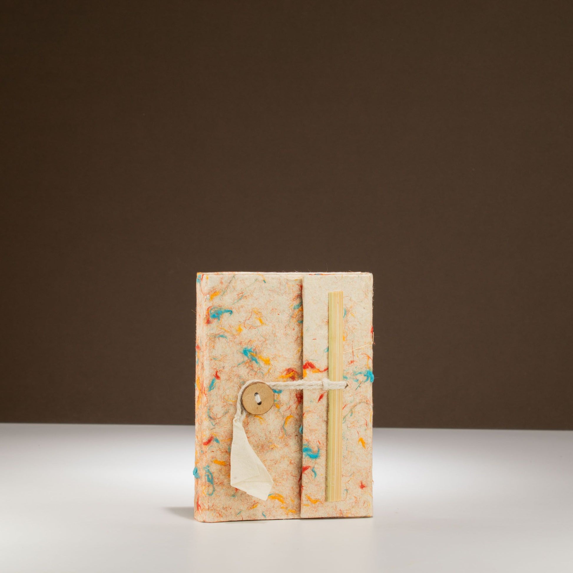 Cuaderno artesanal con tapa de papel reciclado en tonos beige y detalles de colores, cierre con botón de madera.