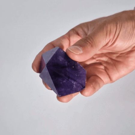 Cristal de amatista morado, de forma irregular, sostenido en una mano, ideal para decoración y propiedades energéticas.