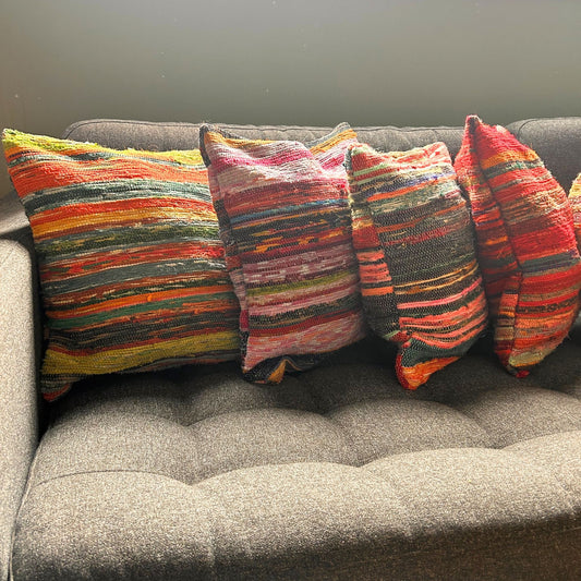 Cuatro fundas para cojín de 40x40cm hechas de tela reciclada a rayas multicolores, sobre un sofá gris.