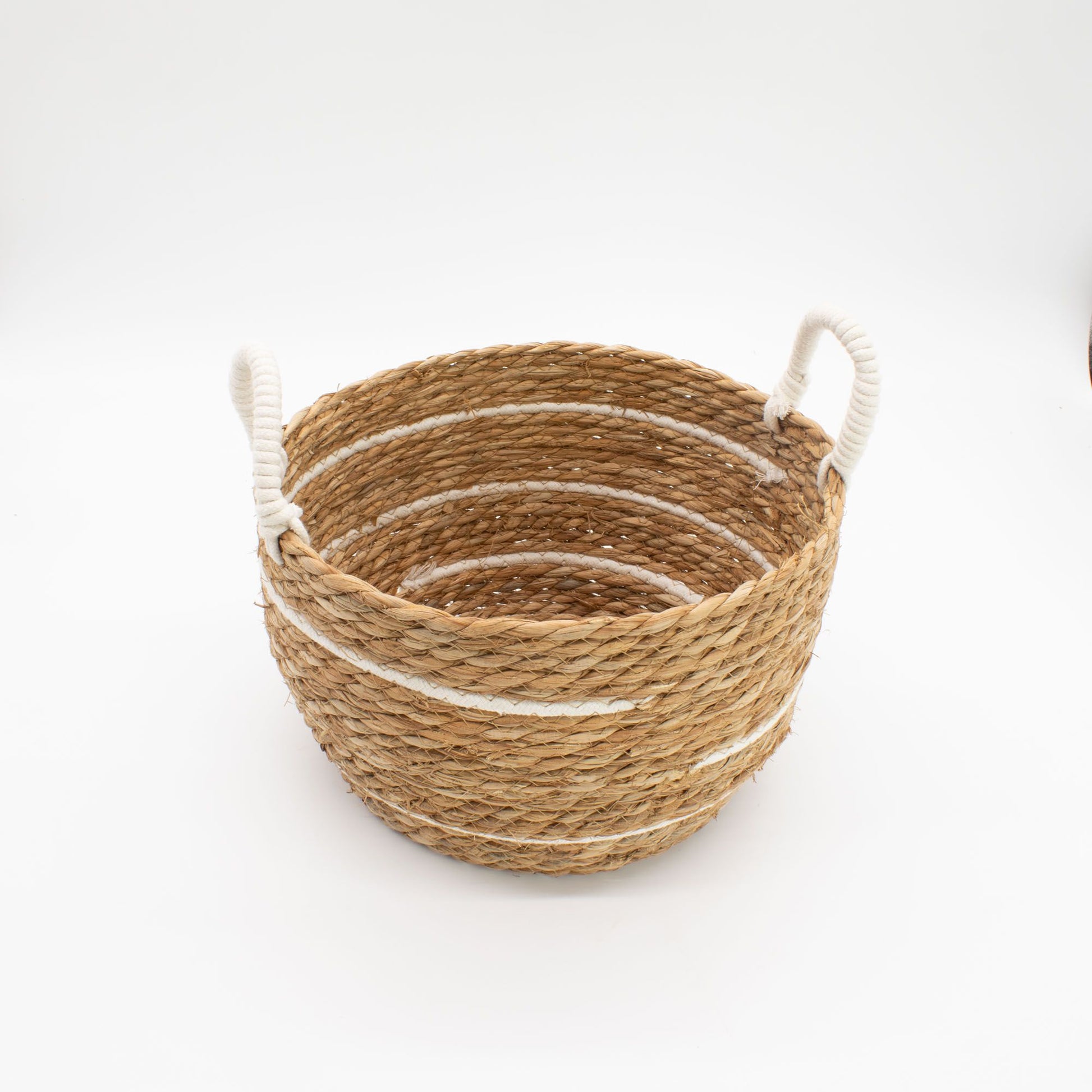 Cesta redonda de pasto marino trenzado con rayas blancas de algodón y dos asas laterales de cuerda gruesa.