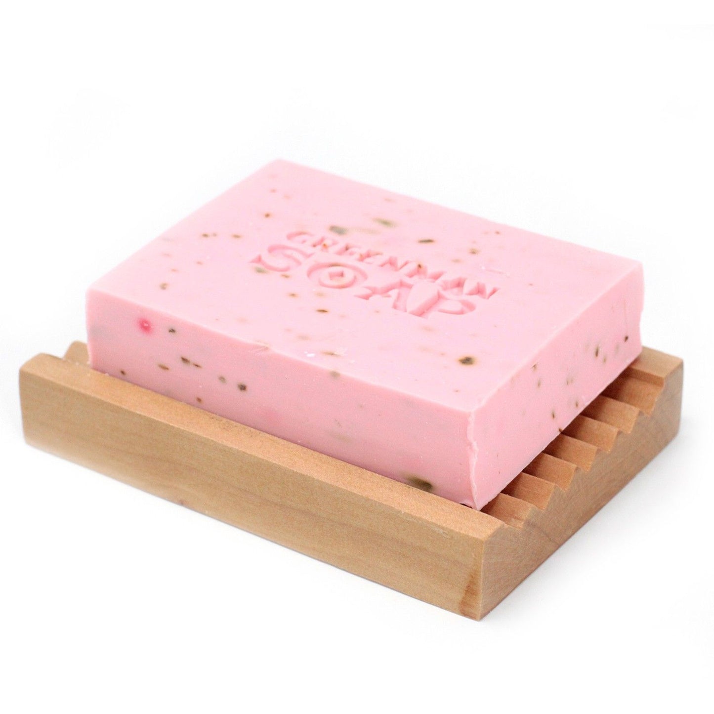 Pastilla de jabón rosa con granos sobre una jabonera de madera clara. Relieve "Greenman Soap" en la parte superior.