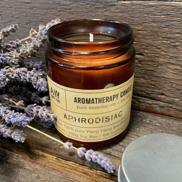 Vela aromática de soja en frasco ámbar, aroma Ylang Ylang, con etiqueta "Aphrodisiac", ideal para relajación.