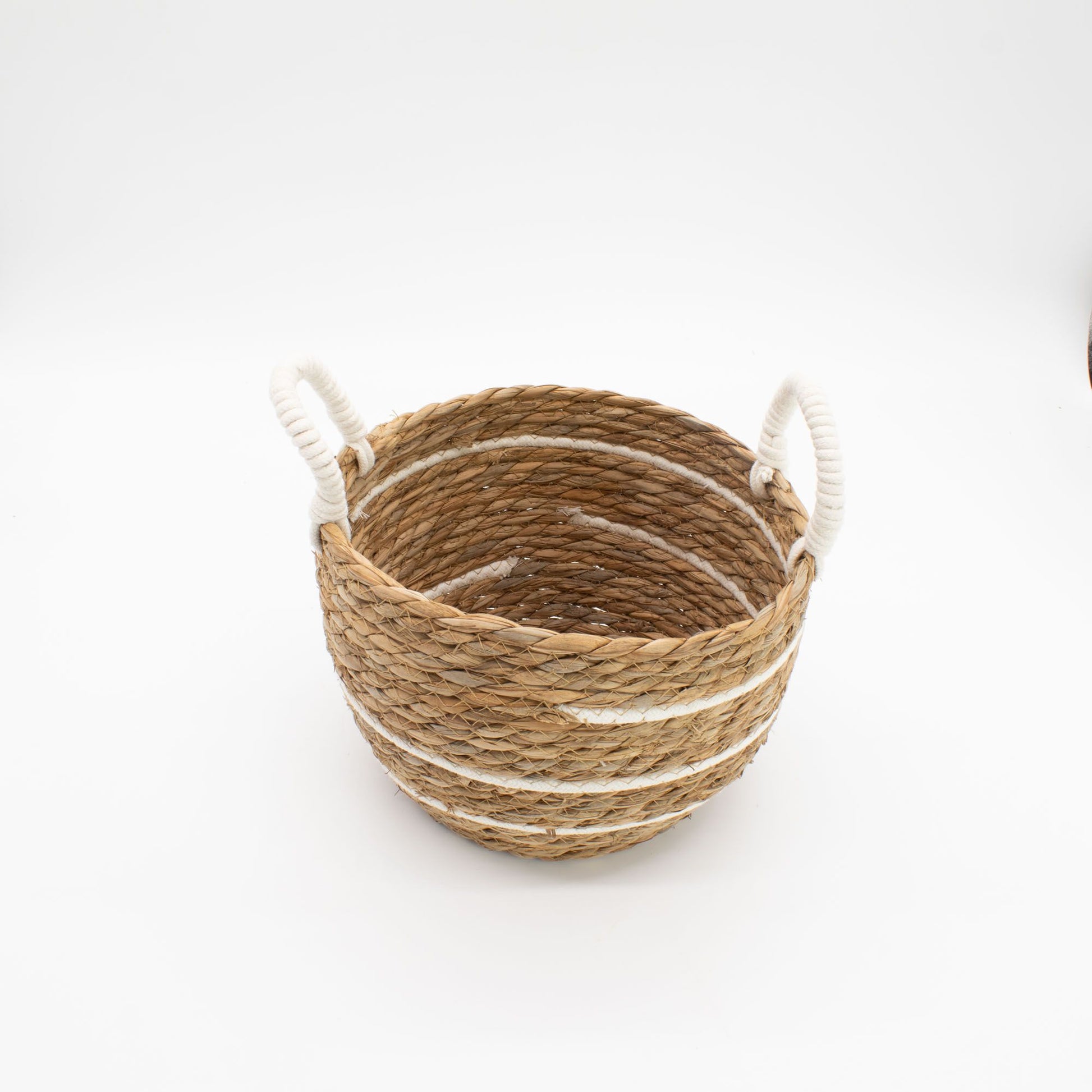 Cesta redonda de pasto marino trenzado con rayas blancas de algodón y asas laterales, estilo natural y artesanal.