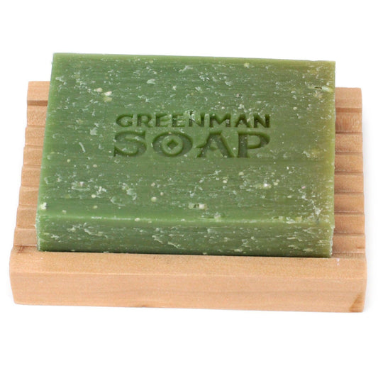 Pastilla de jabón exfoliante verde con textura rústica sobre una jabonera de madera con ranuras.