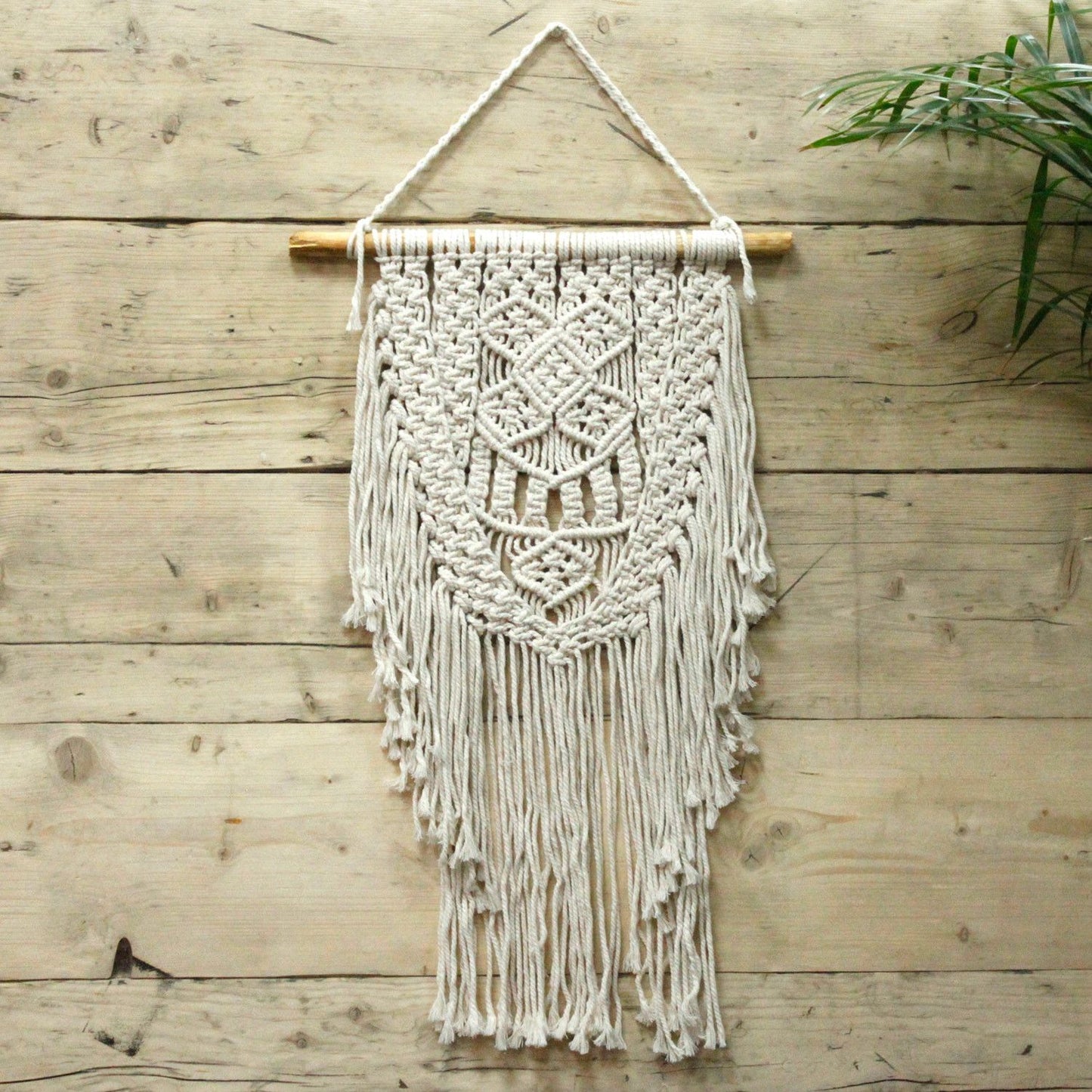 Mural de macramé beige con flecos, hecho de cuerda natural, estilo boho, ideal para decoración de interiores.
