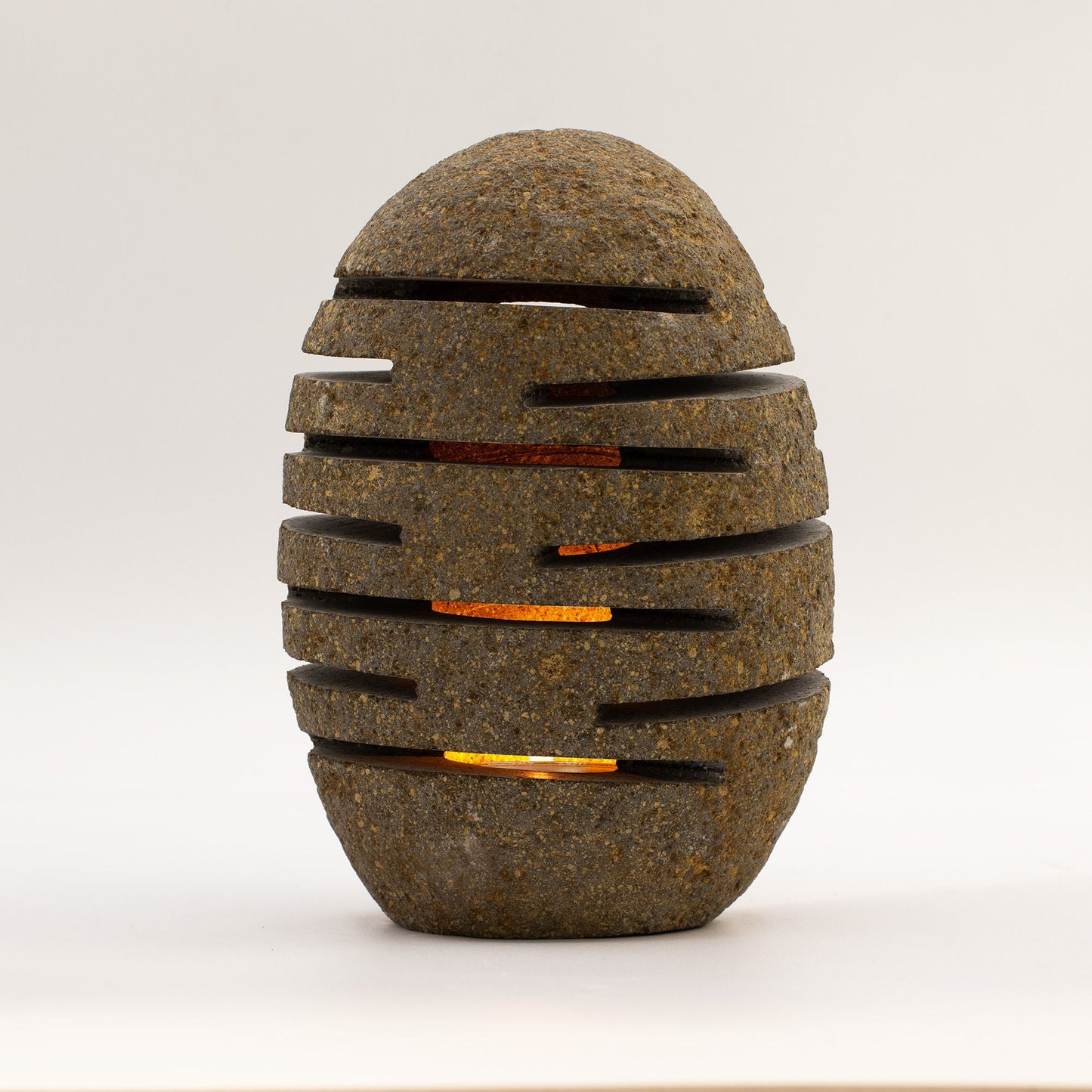 Lámpara decorativa de piedra gris, estilo moderno, con ranuras que emiten luz cálida. Ideal para interior.
