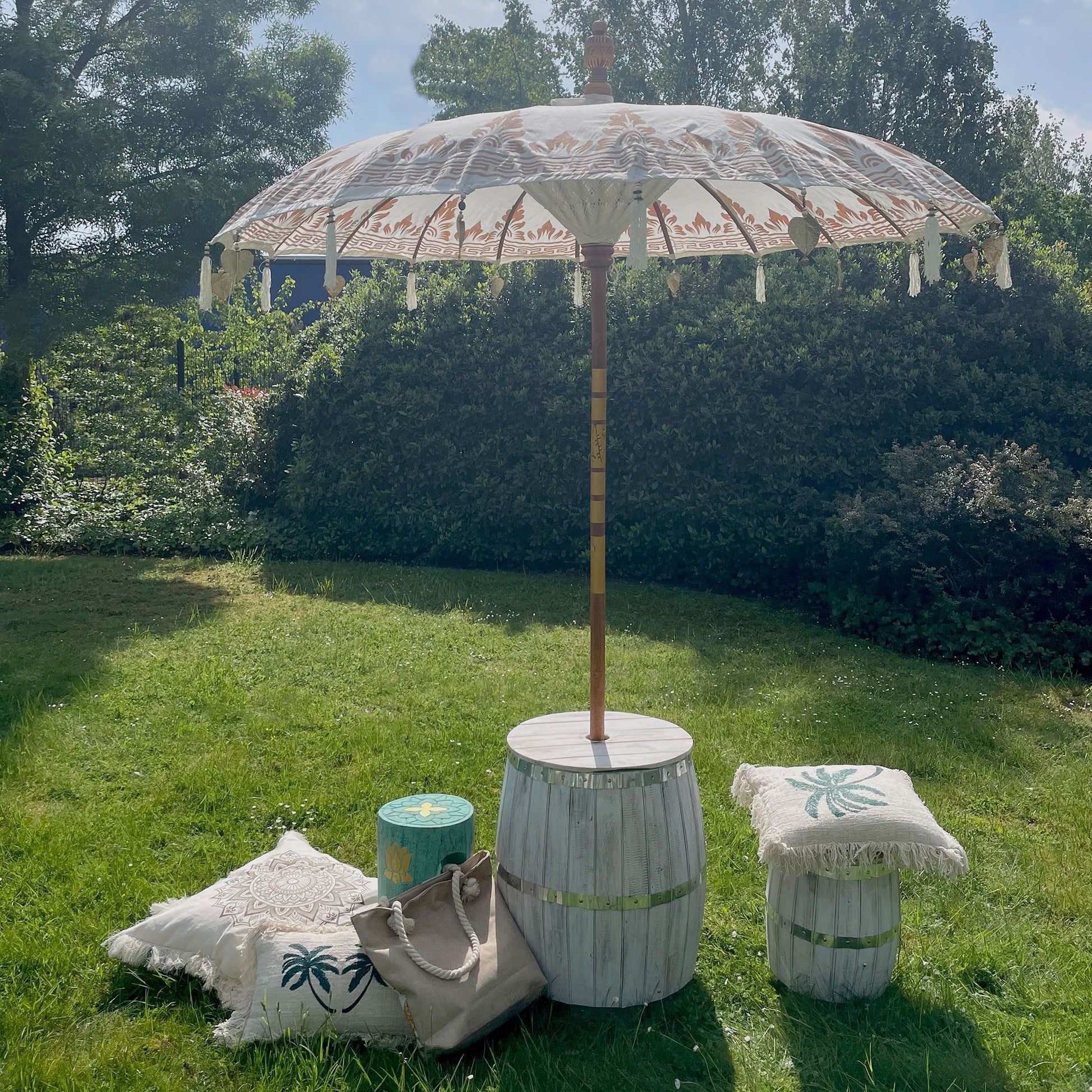 Sombrilla de patio estilo Bali de 2m, lona blanca con detalles dorados y flecos, sobre base de barril de madera clara.