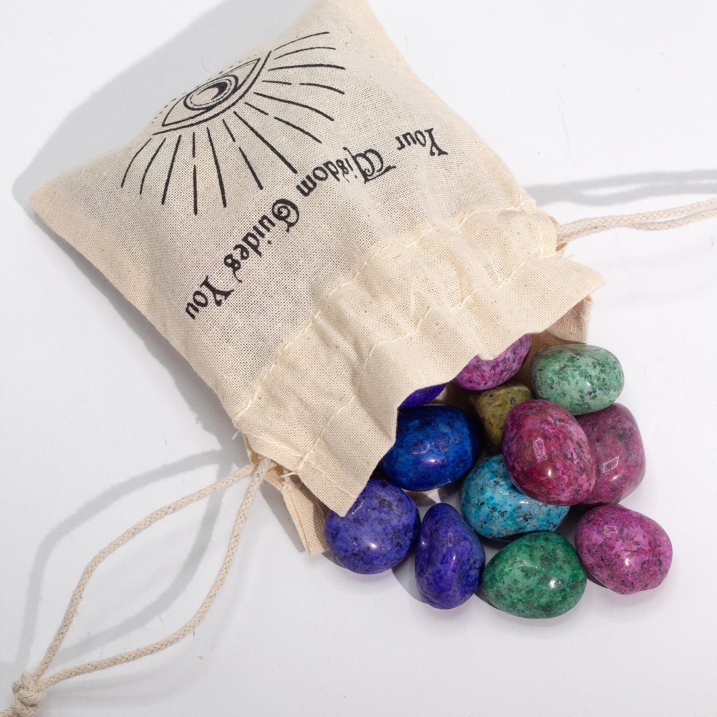 Sacos de tela con piedras de colores vibrantes (morado, azul, verde, rosa) para meditación y armonización.