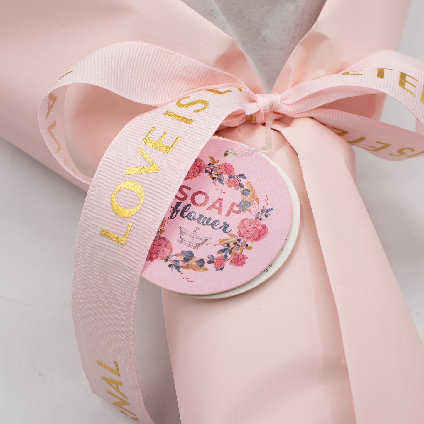 Ramo de flores de jabón en papel rosa con cinta dorada, etiqueta decorativa, estilo elegante y romántico.