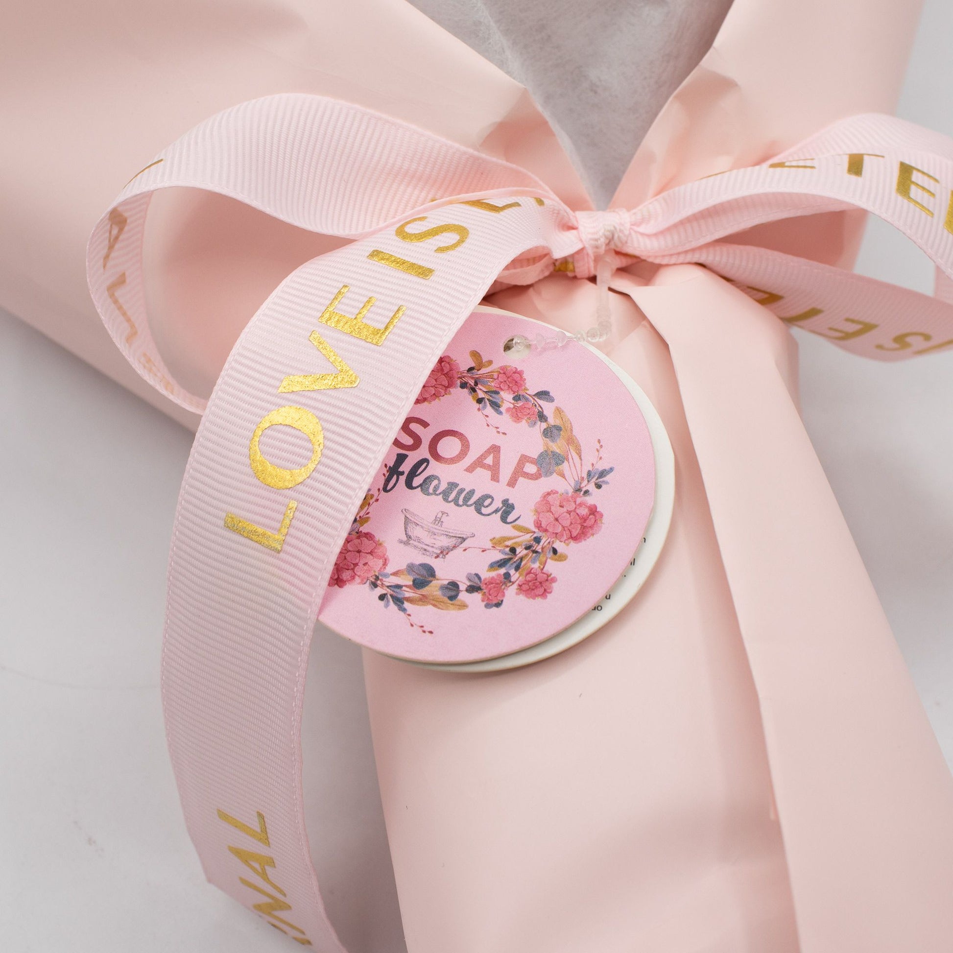 Ramo de flores de jabón en papel rosa con cinta dorada, etiqueta decorativa, estilo elegante y romántico.