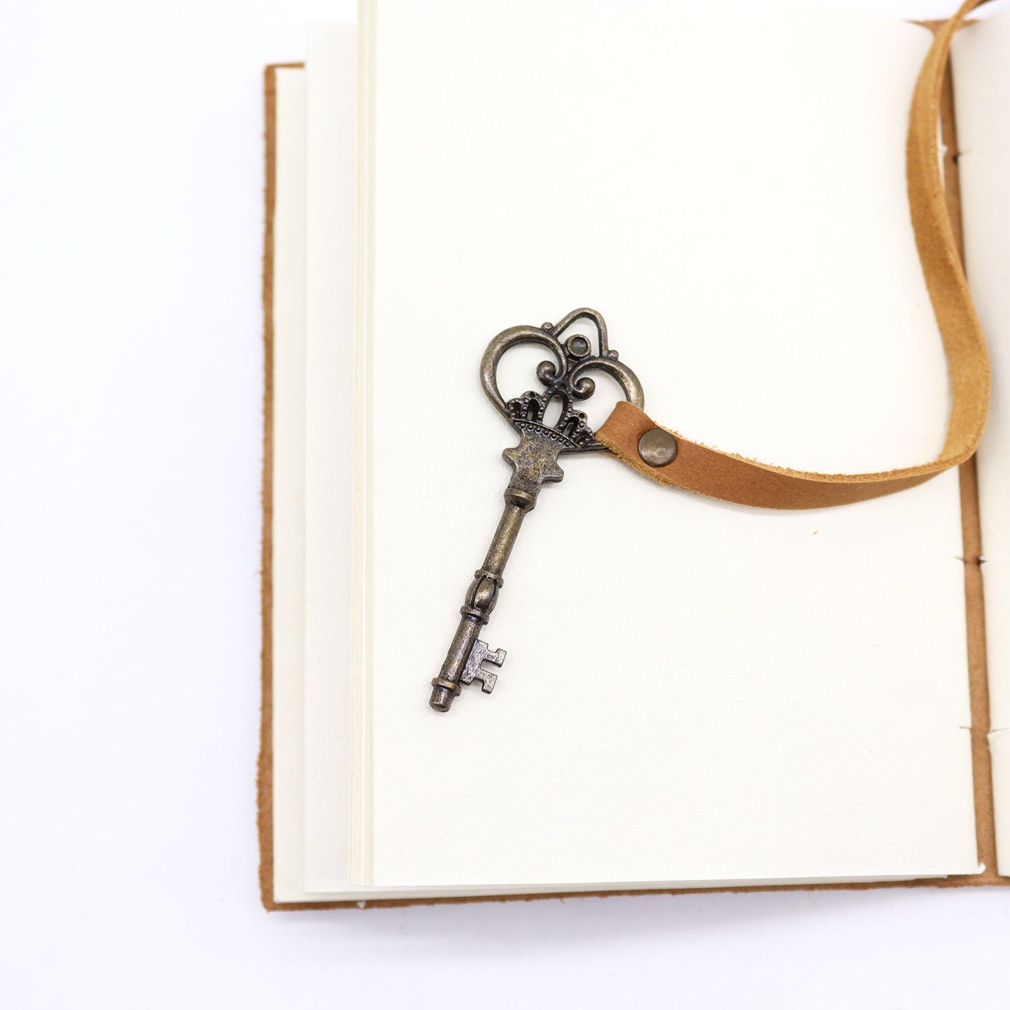 Llave antigua de metal en tonos bronce con cinta de cuero, ideal para cuadernos, estilo vintage.