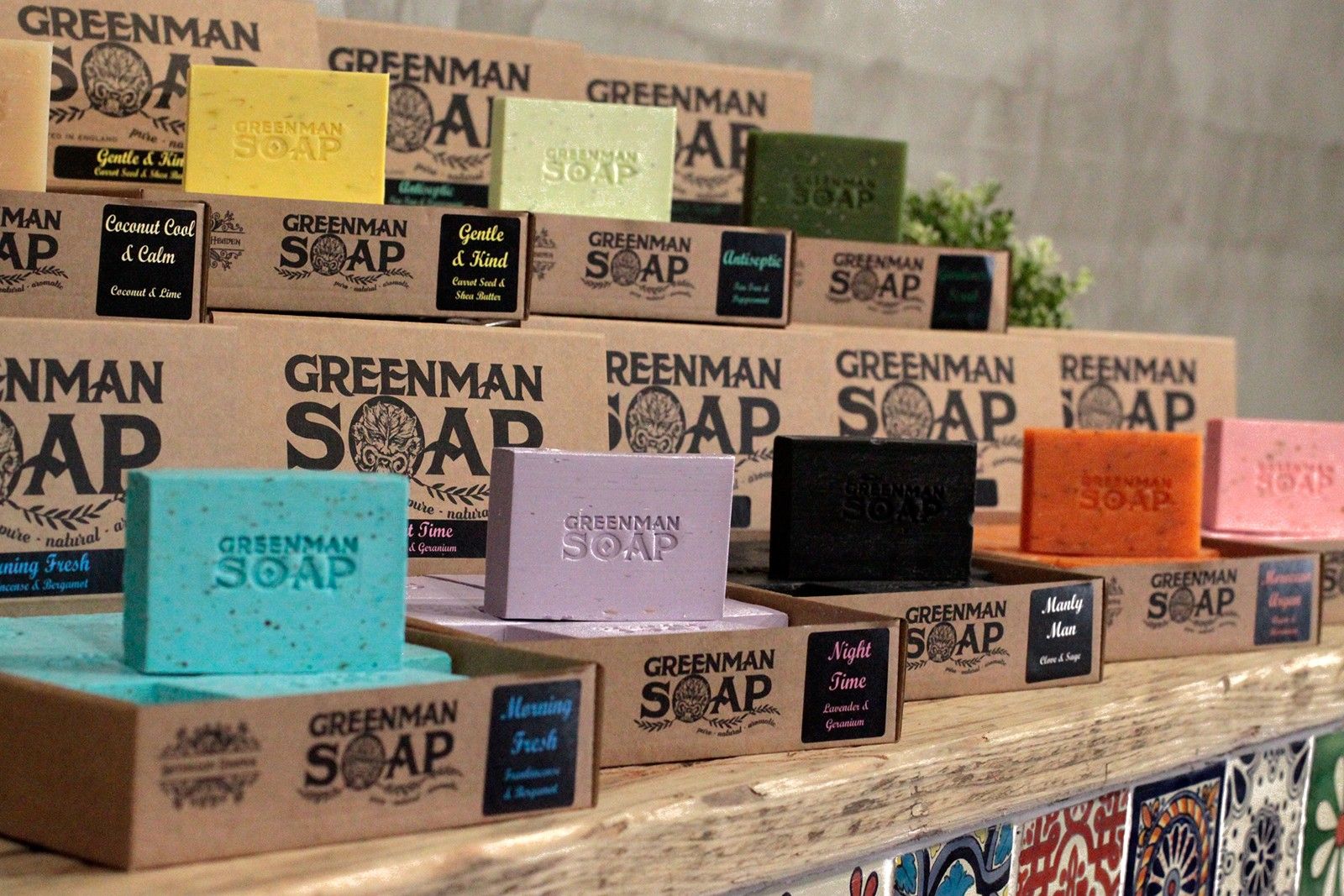 Exhibición de jabones artesanales Greenman en cajas de cartón; destaca el jabón azul "Mañana fresca" en primer plano.