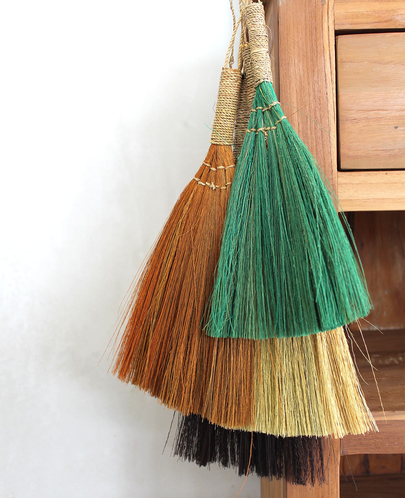Escobas artesanales en tonos naranja, verde, amarillo y negro, hechas de fibras naturales, estilo rústico.