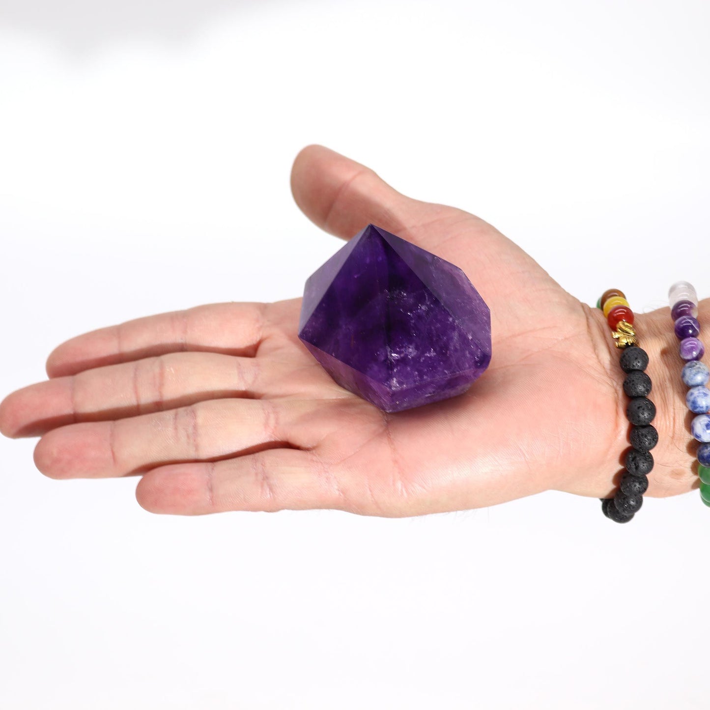 Cristal de amatista púrpura en forma de pirámide, sostenido en una mano. Ideal para decoración y energías positivas.
