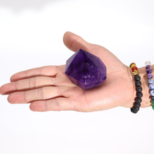 Cristal de amatista púrpura en forma de pirámide, sostenido en una mano. Ideal para decoración y energías positivas.
