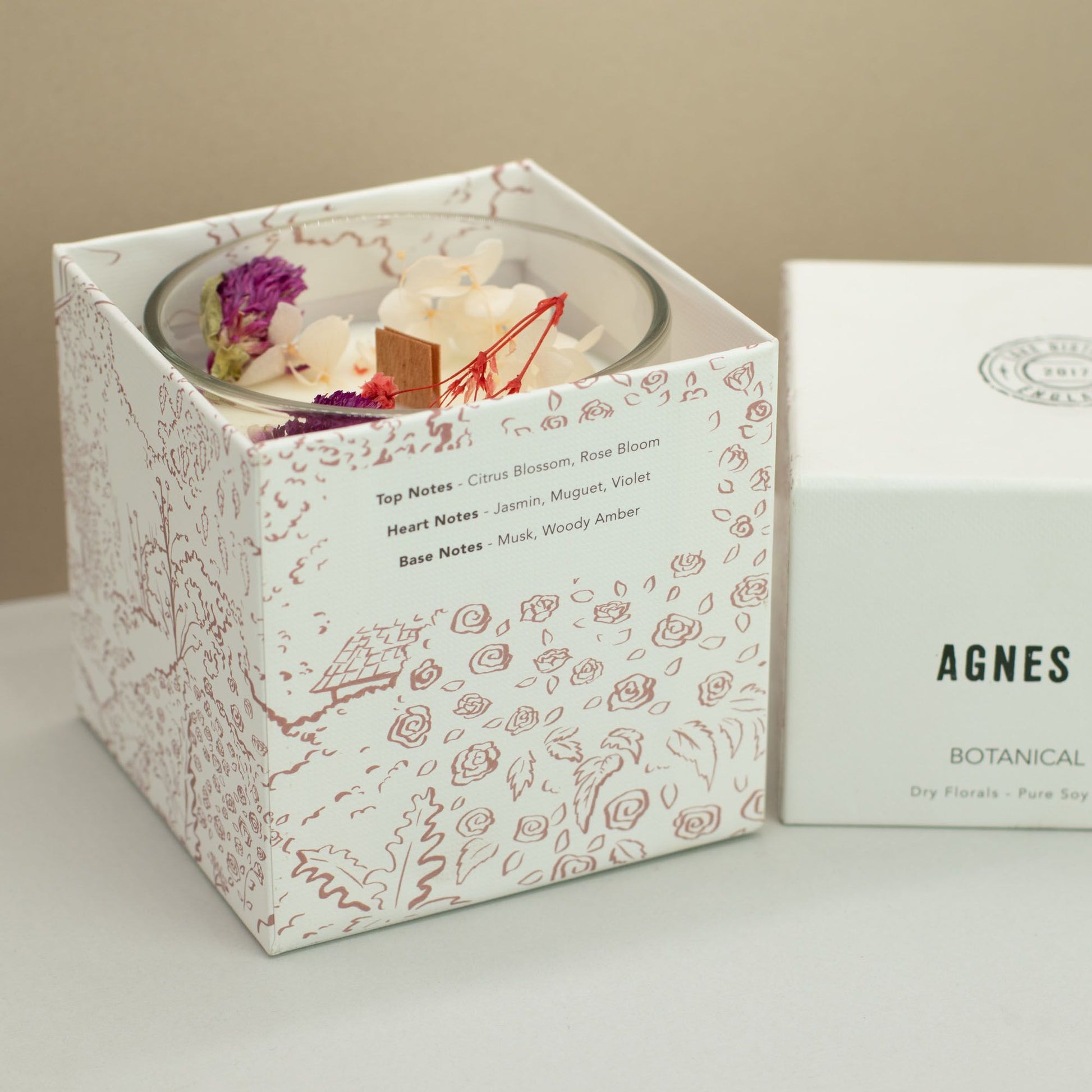 Vela aromática en caja blanca con diseño floral, notas de cítricos, jazmín y madera, ideal para decoración y relax.
