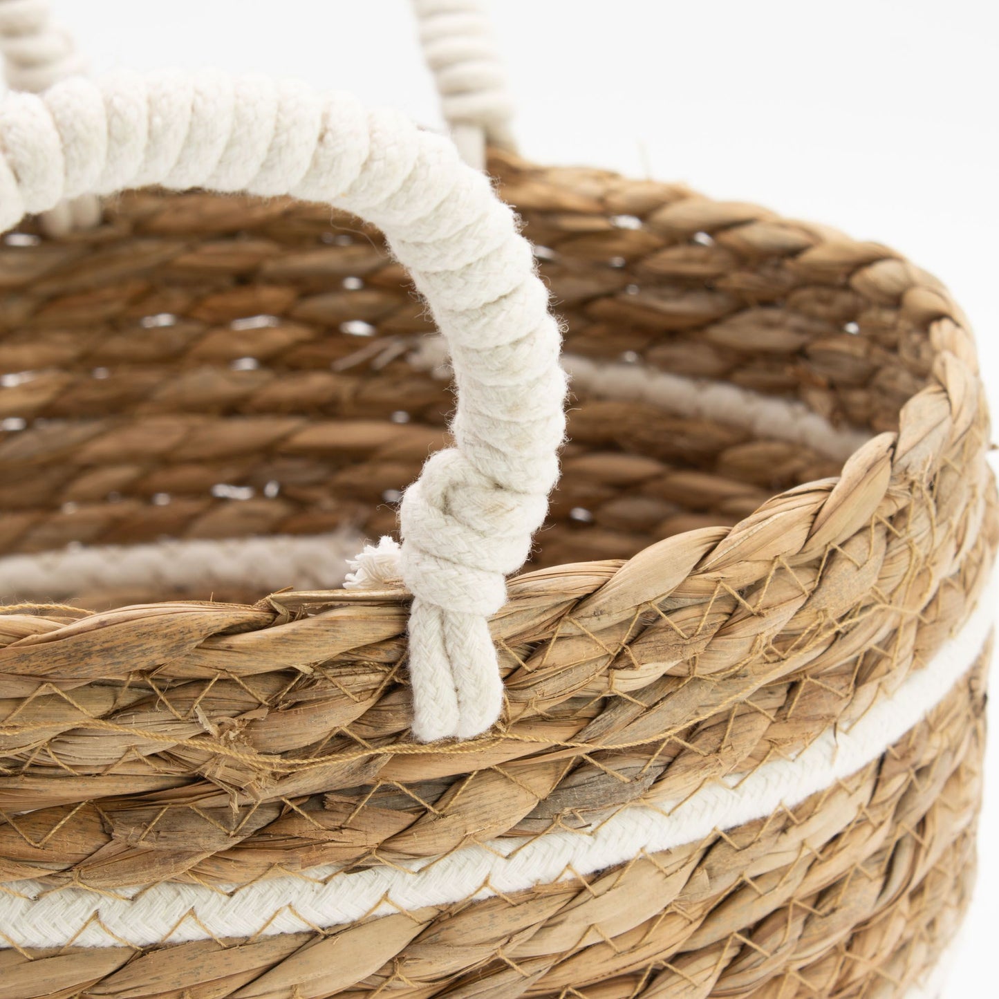 Cesta de pasto marino trenzado con rayas de algodón blanco y asas de cuerda, estilo rústico artesanal.