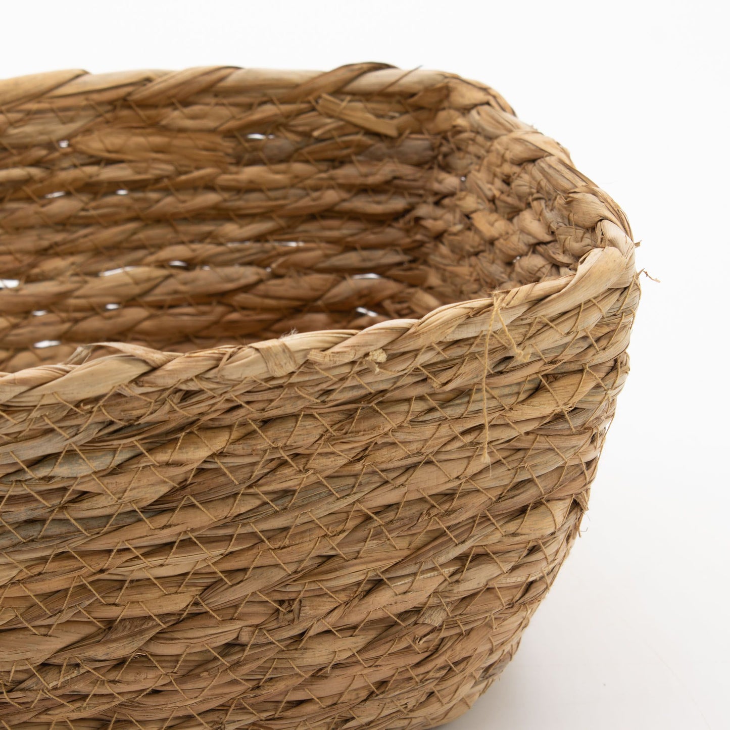 Detalle de cesta cuadrada tejida artesanalmente con hierba marina y hoja de plátano en tonos naturales y rústicos.