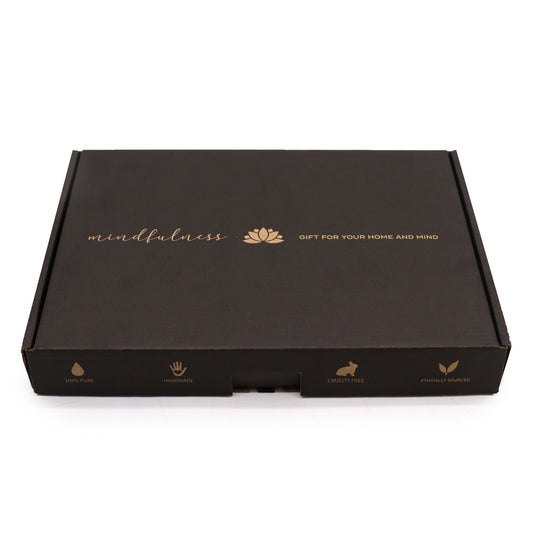 Caja rectangular negra de cartón con letras doradas, icono de flor de loto y sellos de producto ético y artesanal.