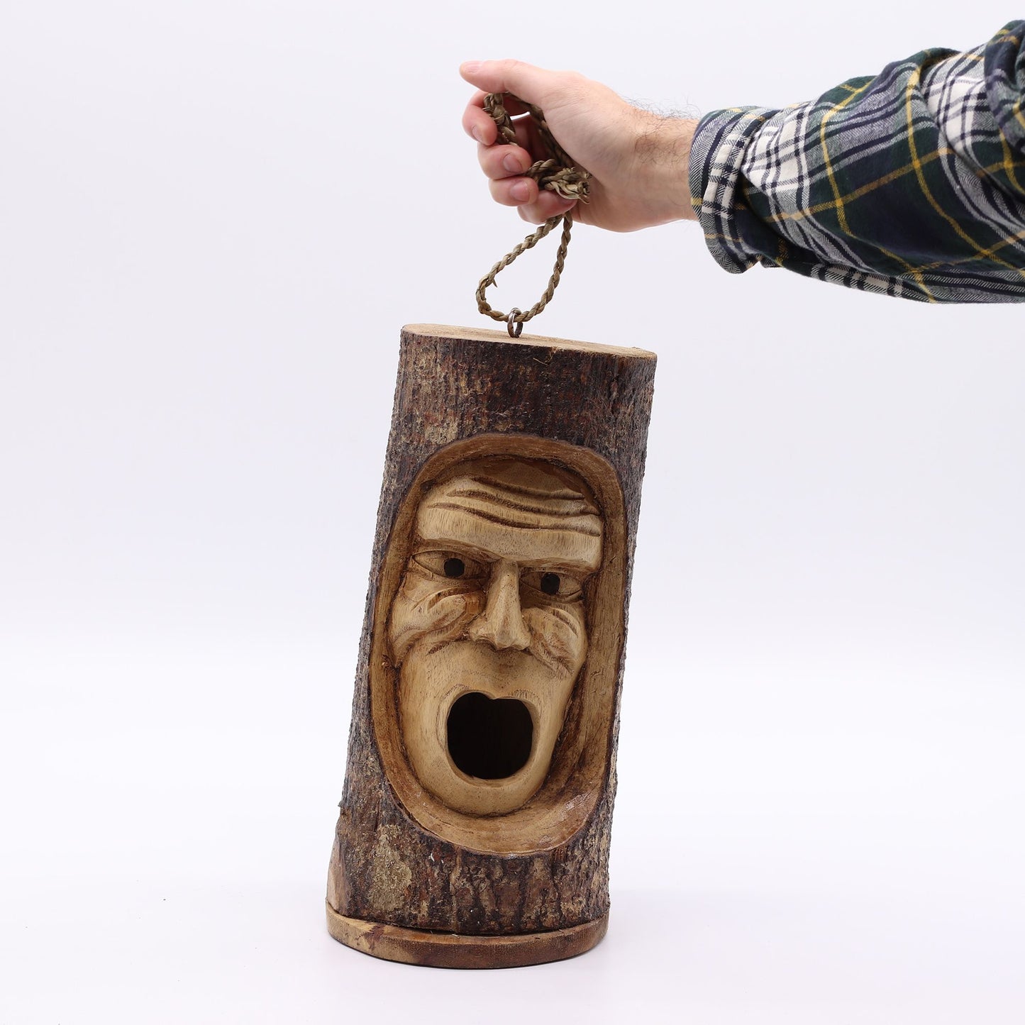 Escultura de madera en forma de tronco con cara tallada, detalles en tonos marrones y cuerda de sujeción.