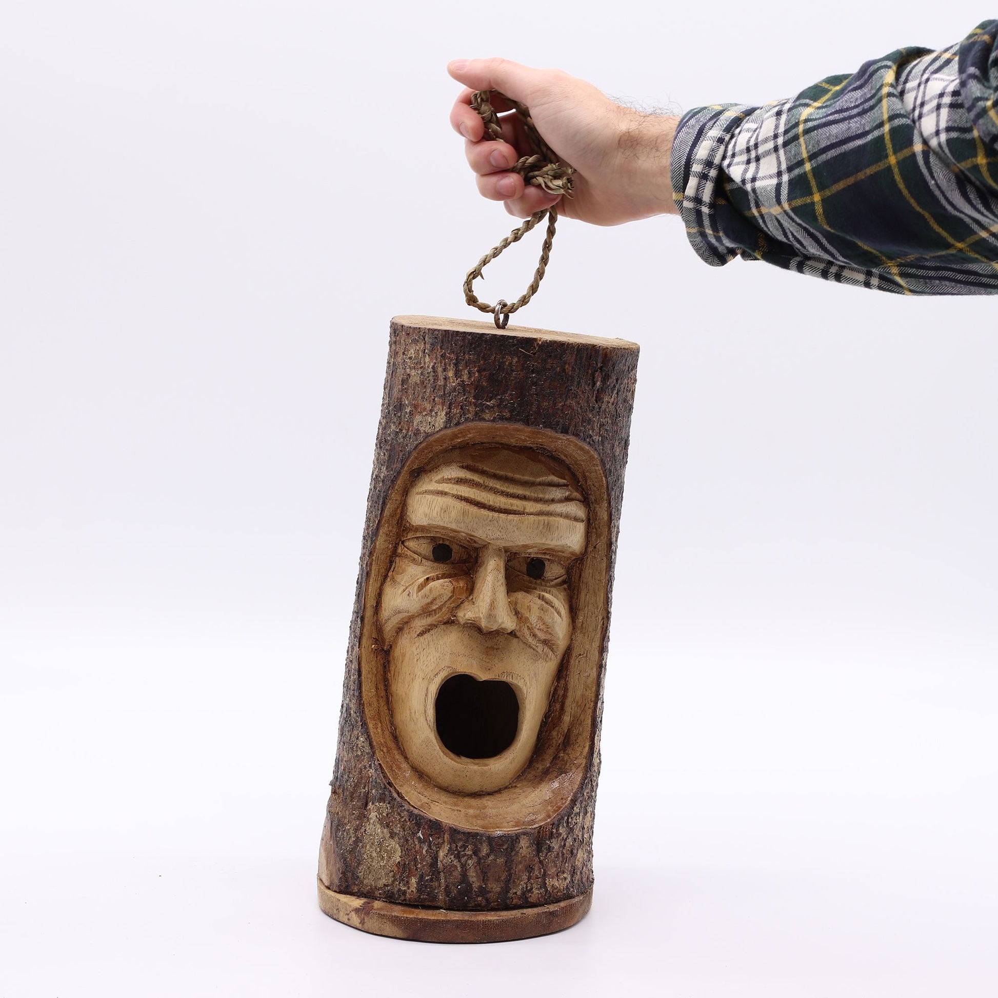 Escultura de madera en forma de tronco con cara tallada, detalles en tonos marrones y cuerda de sujeción.