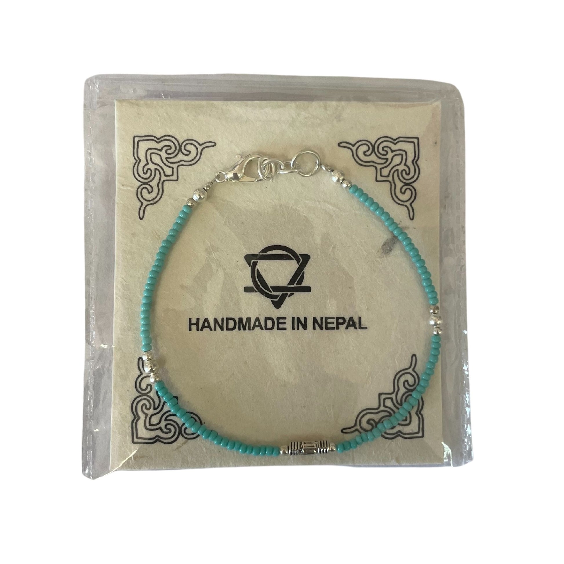 Pulsera artesanal de Nepal, cuentas turquesas y separadores plateados, presentada en empaque decorativo.