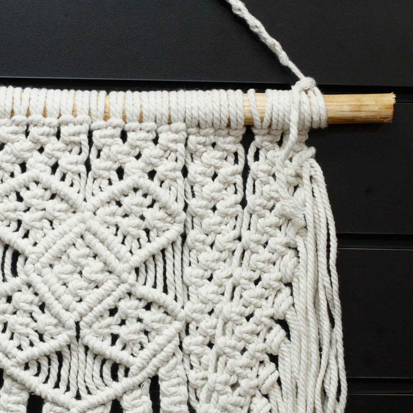 Tapiz de macramé blanco hecho a mano, diseño geométrico y bordes con flecos, decorativo para interiores.