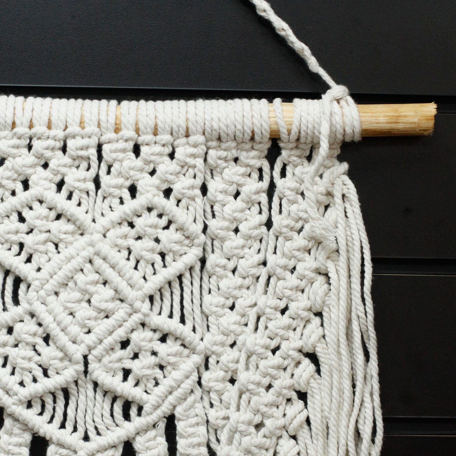 Tapiz de macramé blanco hecho a mano, diseño geométrico y bordes con flecos, decorativo para interiores.