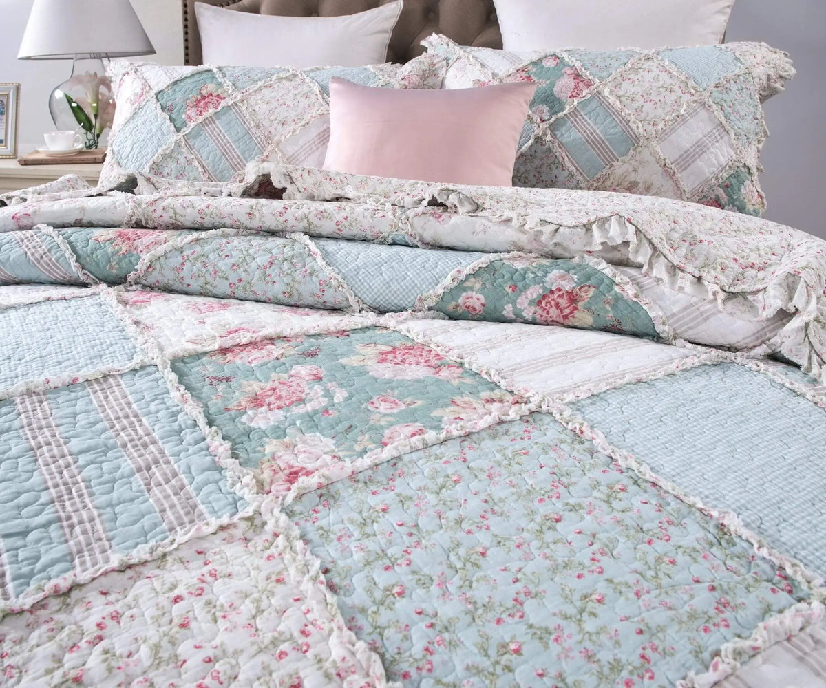 Vintage floral patchwork quilt in soft teal, white, and pink tones with ruffled edges, perfect for a cozy bedroom.