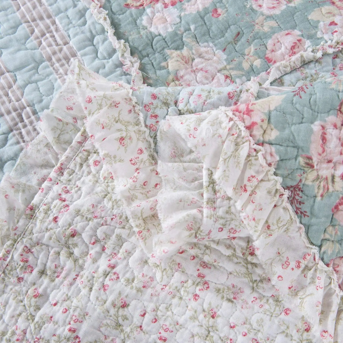 Vintage floral quilt in pastel shades of pink and blue, featuring delicate ruffles and intricate stitching details.