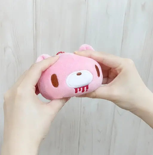 Hands squeezing a pink, plush Gloomy Bear keychain with a red blood drip detail and a metal bead chain.