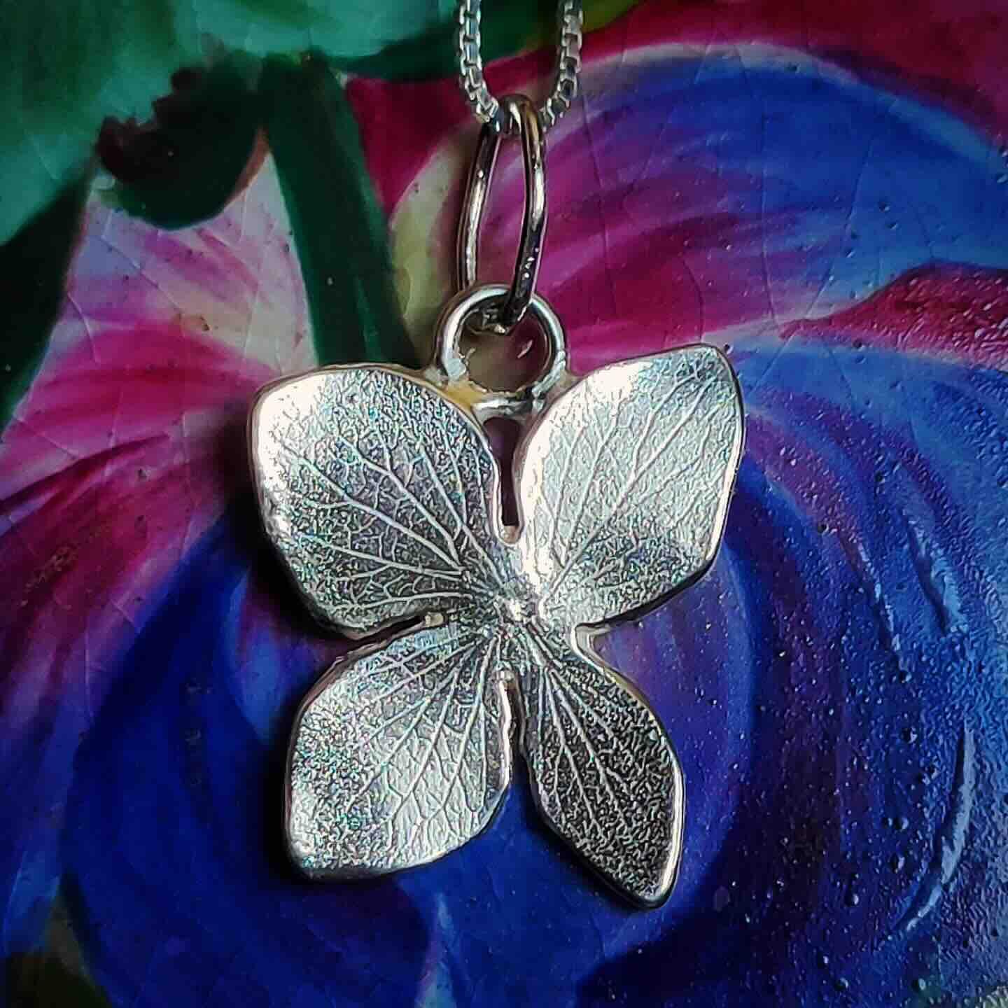 Collar con colgante en forma de mariposa de plata, acabado brillante, sobre fondo colorido.