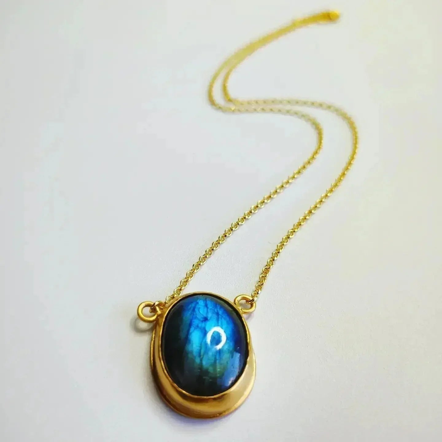 Collar dorado con piedra labradorita azul en forma ovalada y cadena delicada.