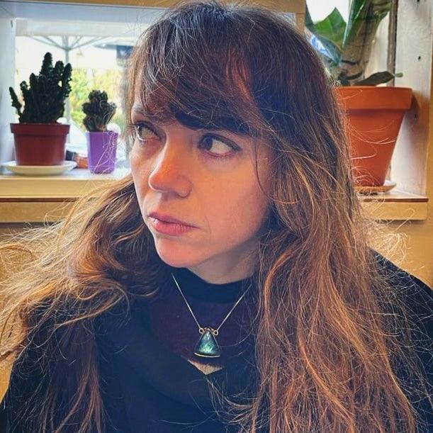 Mujer con cabello largo y suelto, usando un collar de plata con piedra turquesa en un entorno urbano.
