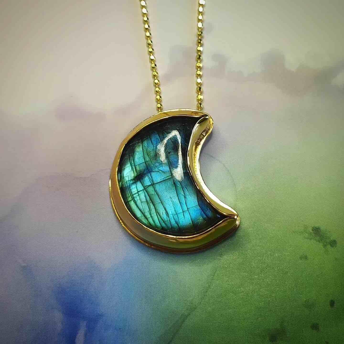 Colgante en forma de media luna de labradorita azul con marco dorado, diseño elegante y moderno.