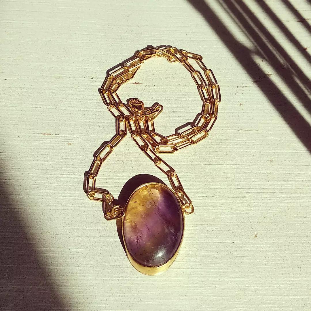 Collar dorado con ónix morado en forma ovalada, estilo elegante y moderno. Ideal para ocasiones especiales.