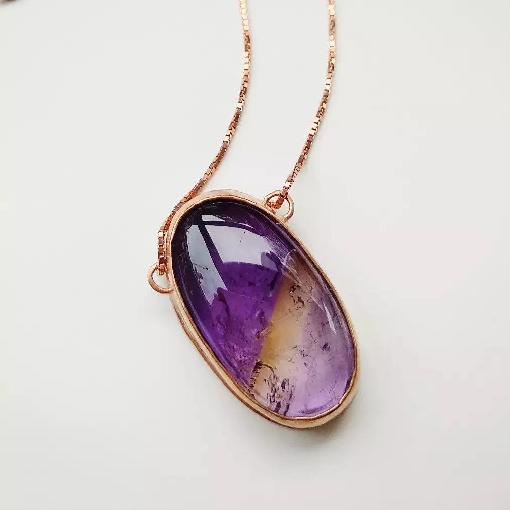 Collar de oro rosa con colgante ovalado de amatista en tonos morados y amarillos, elegante y clásico.