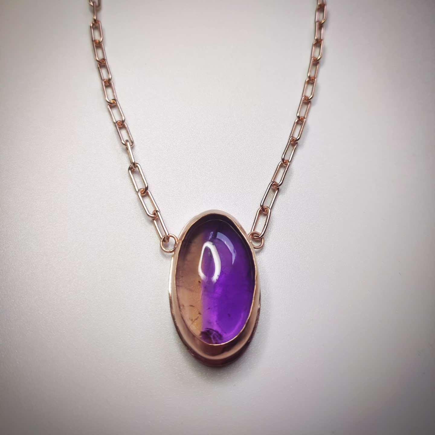 Collar de metal rosa con piedra ovalada de amatista morada. Diseño elegante y moderno.