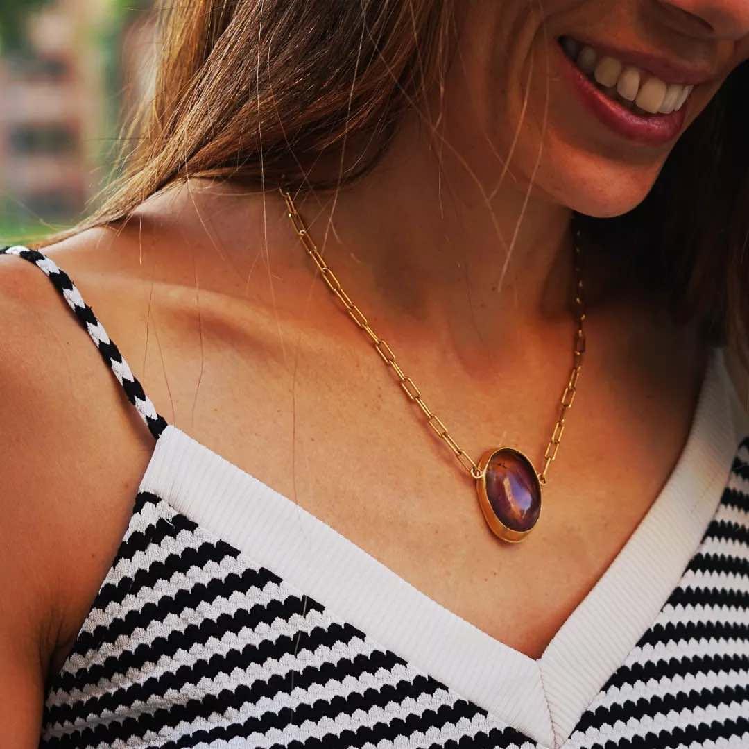 Collar dorado con piedra ovalada en tonos morados, ideal para un estilo elegante y moderno.