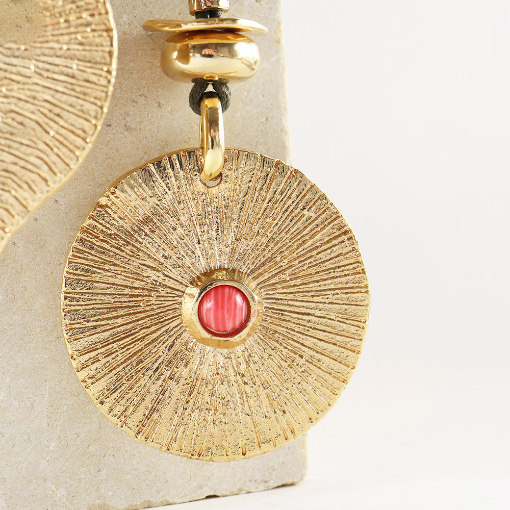Pendientes de oro con diseño radiante y detalle rojo, material de metal y estilo elegante y moderno.