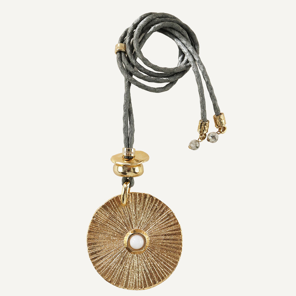 Collar de metal dorado con diseño circular y perla, cordón gris trenzado y detalles en dorado.