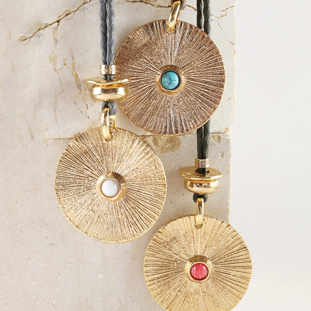 Collares de colgante dorado con detalles en turquesa, blanco y rojo, estilo bohemio, sobre base de piedra.