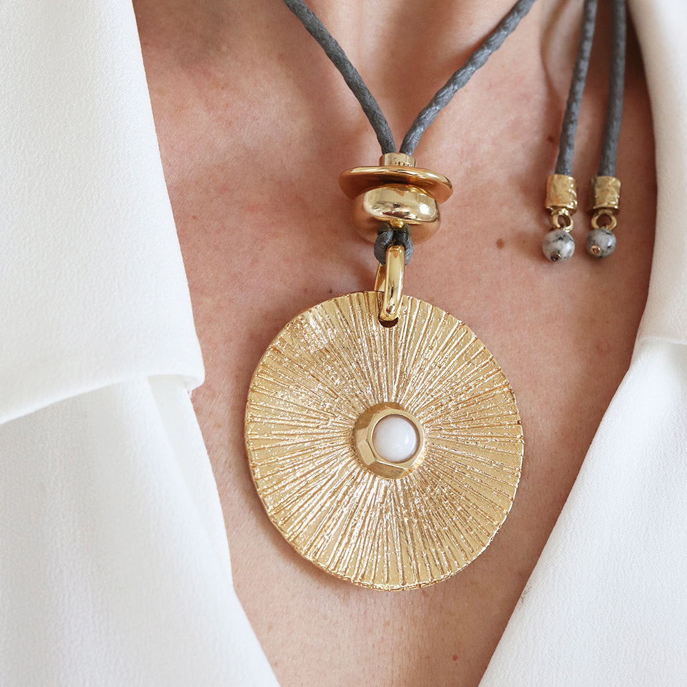 Collar bohemio dorado con colgante redondo, perla central y cordón de cuero gris. Perfecto para un look elegante.