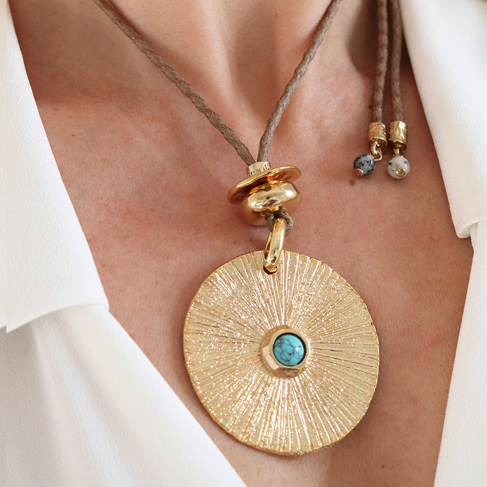 Collar bohemio con colgante dorado, bisel de turquesa y cordón marrón, estilo moderno y artesanal.