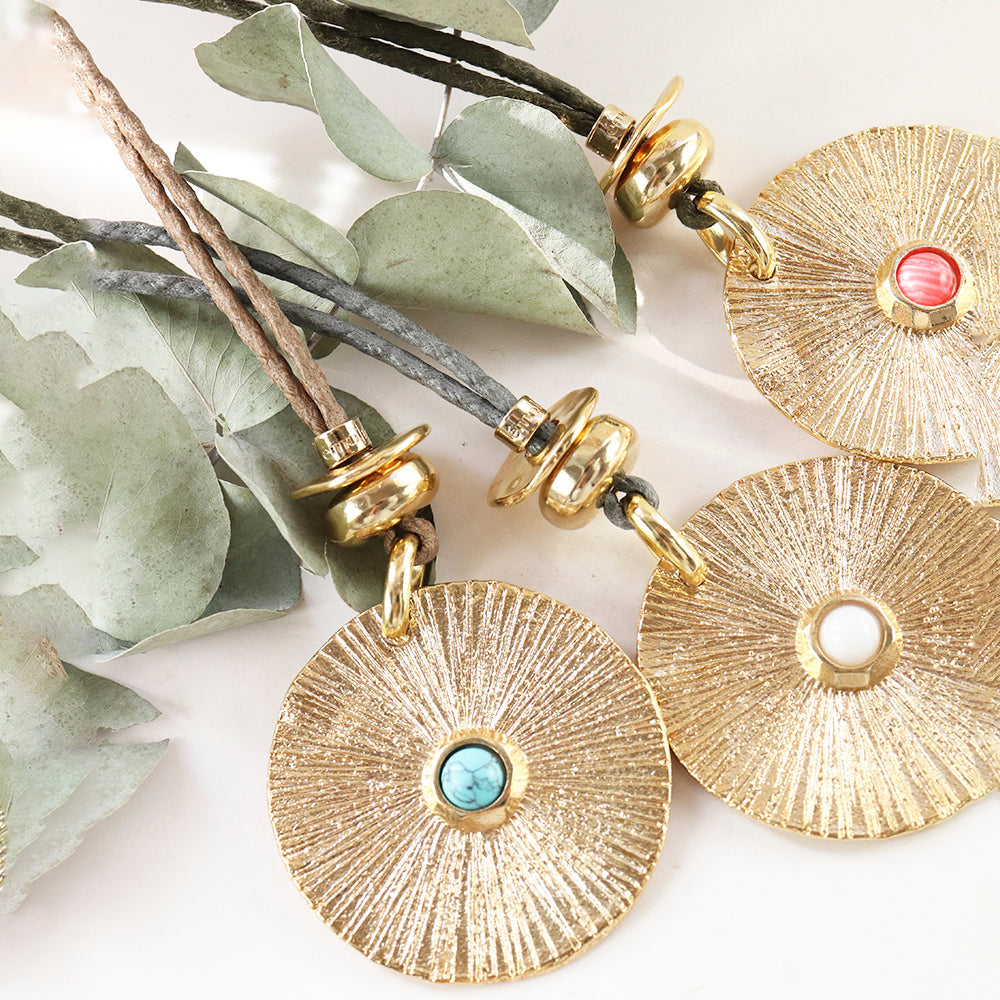 Collares de estilo bohemio con medallas doradas y piedras turquesas, rojas y blancas, sobre cuerdas en tonos naturales.