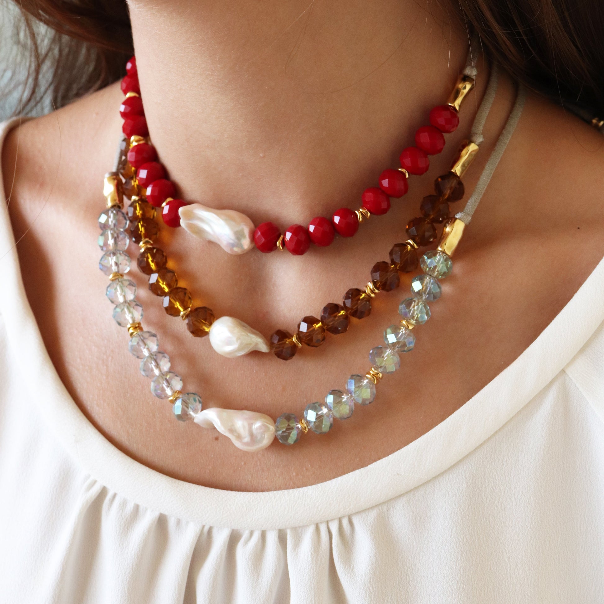 Collares de perlas y cristales en tonos rojo, ámbar y azul, con diseño elegante y femenino.