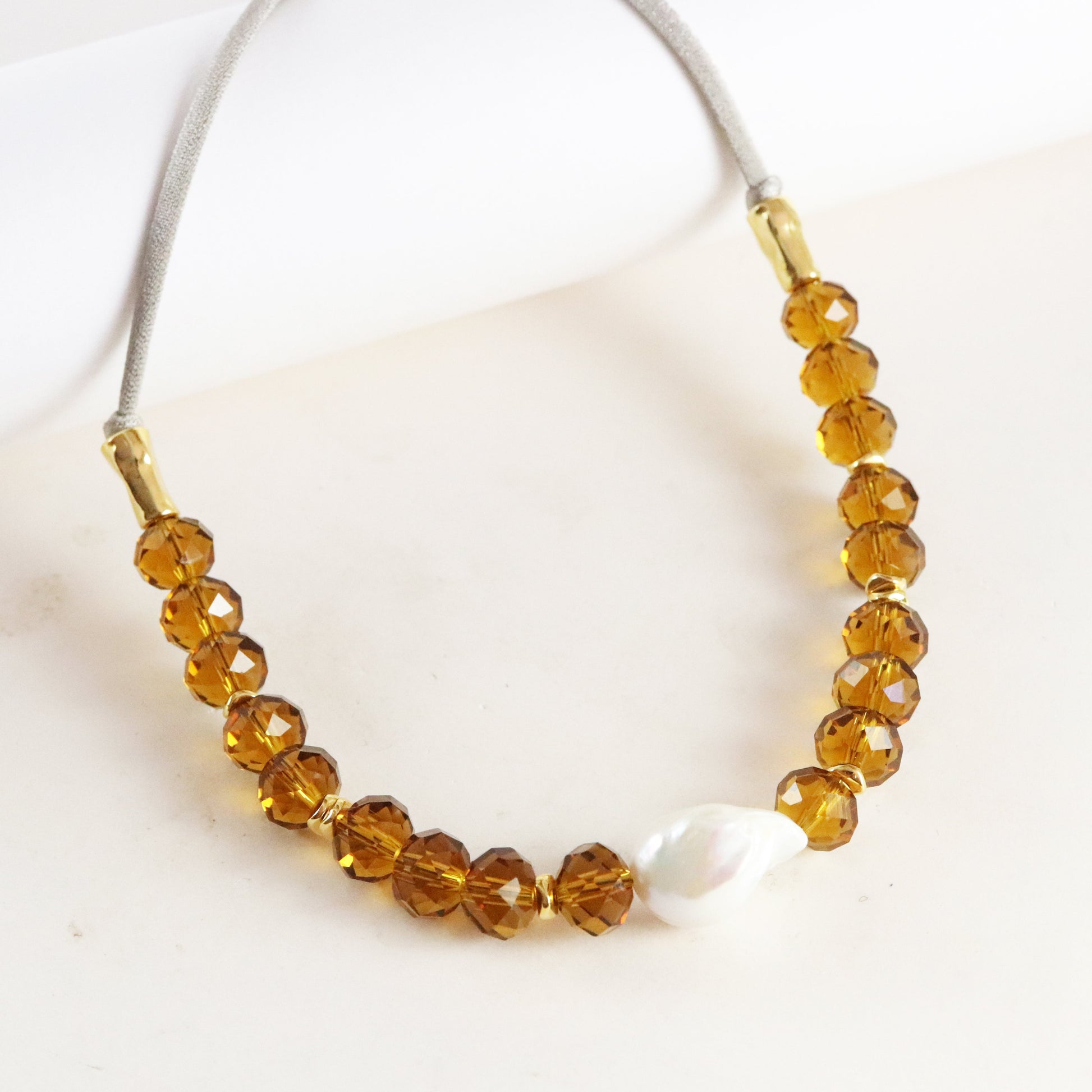 Collar de cristal ámbar con perla, estilo moderno y elegante, cierre dorado y cordón gris.